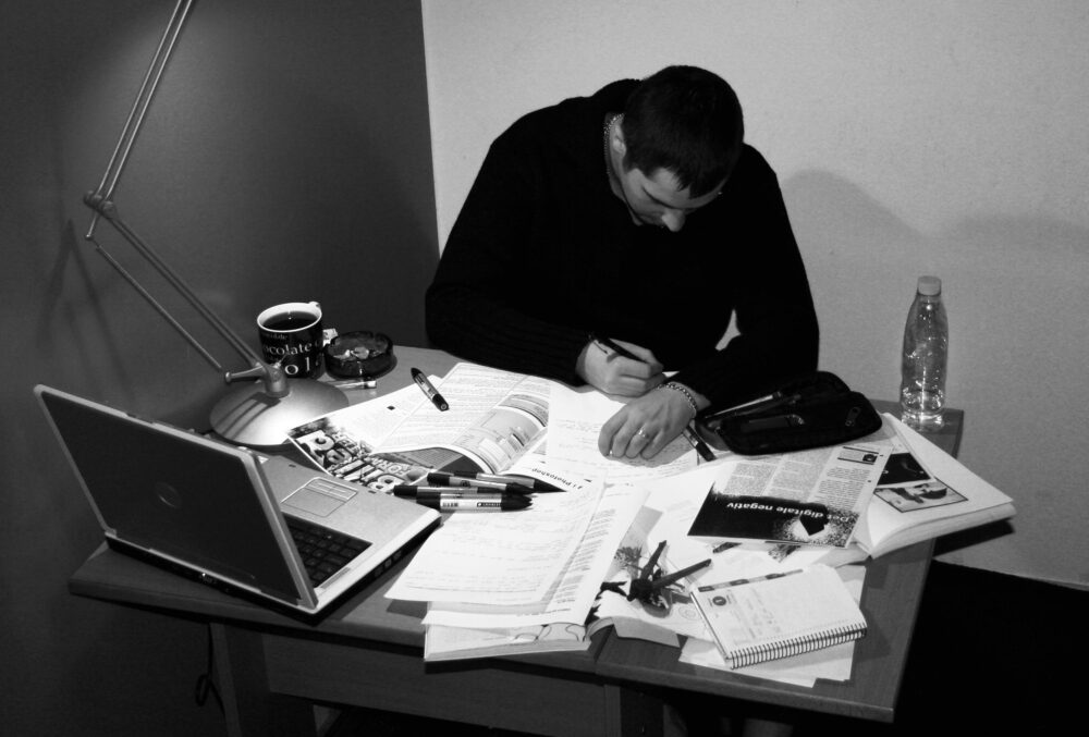 Student sedící u stolu s mnoha učebními pomůckami