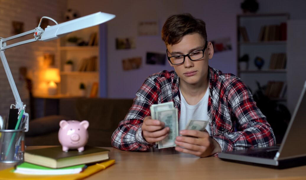 Teenager counting dollar bills and putting them to piggyback, first salary