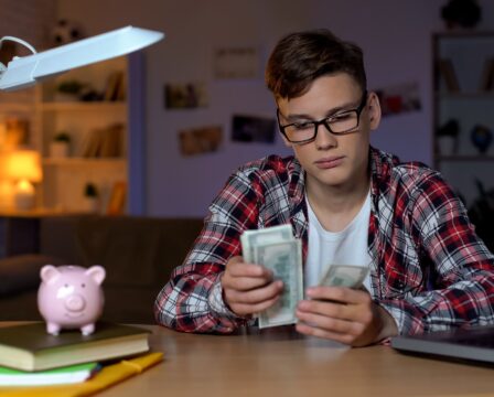 Teenager counting dollar bills and putting them to piggyback, first salary